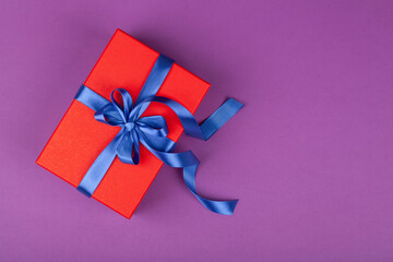 red gift or present box with blue ribbon on violet background.