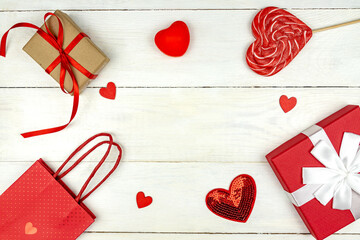 Creative Valentine Day romantic composition with red hearts, satin ribbon, lollipop, gift box and paper bag on white background. Mockup with copy space for blogs and social media.