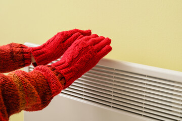 Woman warming hands at radiator. Concept of heating season
