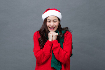 Portrait of smiling excited asian woman wearing christmas sweater with hands together under chin on isolated gray studio background