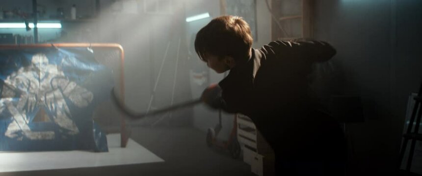 Kid boy hockey player practicing shots inside a covered garage at home. Shot with 2x anamorphic lens