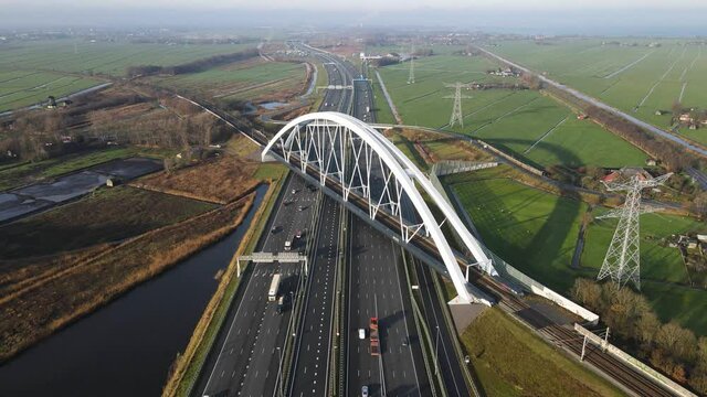 Zandhazenbrug arch bridge over the A1 highway in Muiderberg, The Netherlands Aerial view from above with traffic going under the bridge and a train crossing