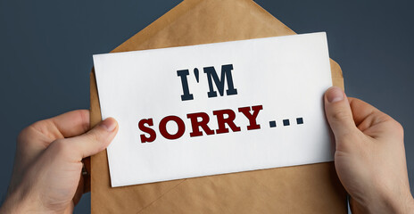 Male hands holding craft envelope with word SORRY on blue background