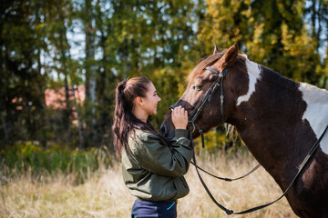 Cute girl talking with her horse after a joint walk in the background of the forest.
