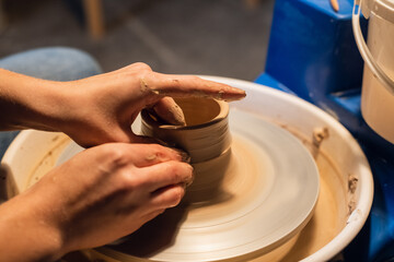 in the workshop, a potter hands sculpts a vase from clay on a potter's wheel
