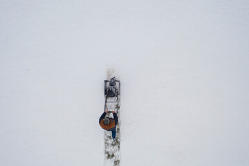 Aerial view snowblower at work on a winter day. Man removing snow after blizzard snowfall. Gardener...