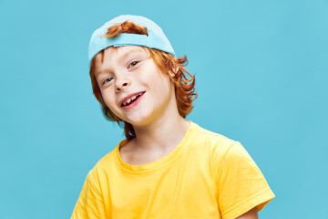 Cheerful red-haired boy in a yellow t-shirt with a blue cap on his head childhood smile 