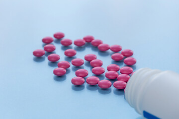 Medical bottle with pink pills isolated on a blue background. Medical health or drugs addiction concept.