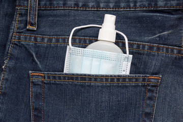 Protective face mask and hand sanitizer spray are lying in back pocket of jeans. Concept for new lifestyle after pandemic.