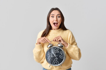 Surprised young woman with alarm clock on grey background