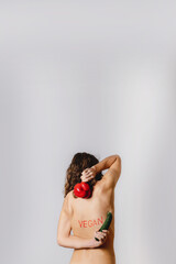 Copy space vertical close-up naked back of woman portrait showing a red vegan write on the skin and holding a sweet pepper and a zucchini. Healthy lifestyle, diet and vegetarian concept.