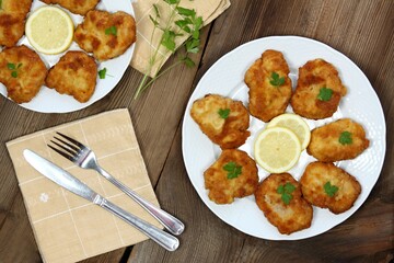 Pork schnitzels served on the plate. Decorated with sliced lemon and parsley. Brown rustic table. Top view, flat lay.