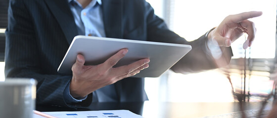 Cropped shot of businessman hand holding tablet and pointing to screen of computer.