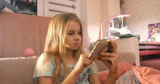 Little girl enjoys playing on smartphone phone in pink room art noise