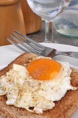 Oeuf au plat sur une tranche de pain de mie servis dans une assiette avec une fourchette en gros plan