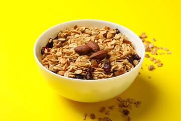 Bowl with granola with nuts and raisins on yellow background