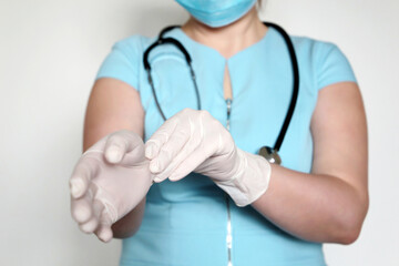Woman in disposable mask puts on her latex gloves. Doctor on medical exam, concept of covid-19...