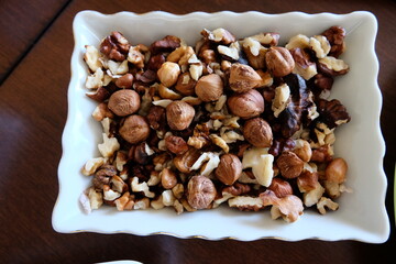 Mix nuts in a small plate. wooden background. Place for text. Assortment of nut in white bowl on dark table. Hazelnuts, walnuts, almonds. It is called 