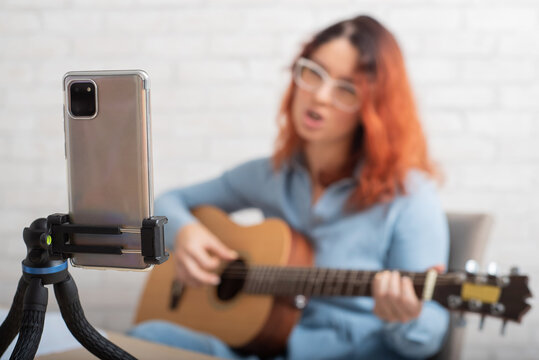 A woman is broadcasting online on her phone at home. The girl sings and plays the guitar live