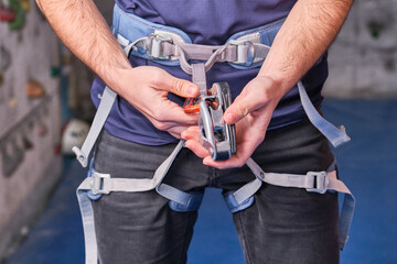 Close-up of climber with climbing equipment, tying snap hook on safety climbing harness, preparing...