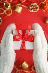 Hands in white knitted mittens holding a gift on a red background.