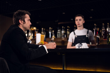 a young man drinks a cocktail at the bar, communicates with the bartender.