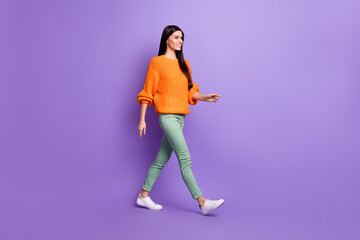 Fototapeta na wymiar Full length body size photo of young girl walking forward in green pants sweater looking copyspace isolated on vivid purple color background