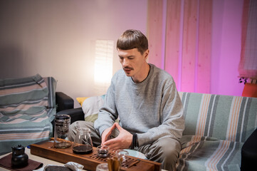 A young adult man learns the art of meditation during a tea ceremony to relax and enjoy the natural aroma of chinese black raw tea