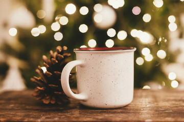 Cup of tea and pine cone on rustic wooden background at Christmas tree lights bokeh. Merry...
