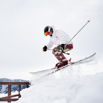 Young man skier in white winter jacket sliding down snow-covered slope on skis. Man freerider in ski suit and helmet skiing on fresh powder snow in mountains. Concept of winter sport activities.