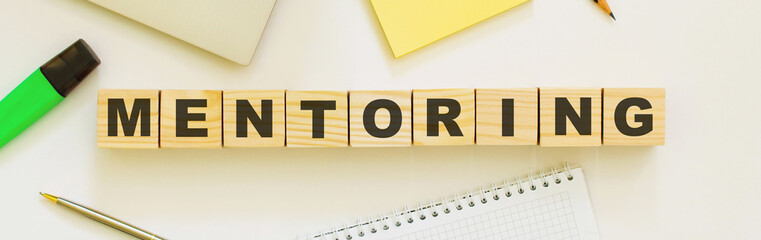 Wooden cubes with word MENTORING on the office desk. Folder and other office supplies.
