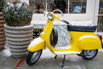 Old classic vintage yellow motor scooter covered snow on winter city background