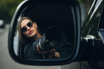 Private detective with camera spying from auto, view through car side mirror