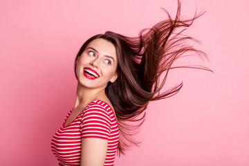 Photo of young attractive smiling cheerful cute girl look copyspace with flying hair isolated on pink color background