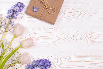 A gift box wrapped in craft paper and blue hyacinth flowers, white roses on a white table top. Flat lay. Copy space for text