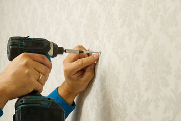 home worker drives the screw into the concrete wall using electric screw driver.