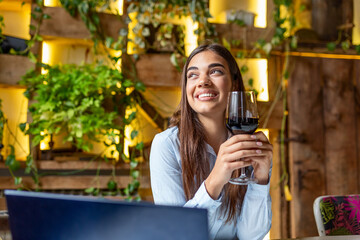Woman works with glass of red wine and laptop in cafe. Woman using laptop while having wine at restaurant. freelancer