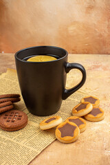 Top view of different biscuits and tea in a black cup on mixed color background