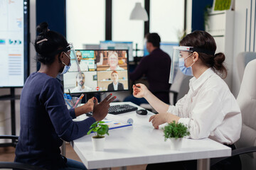 Manager and black woman having a conversation during video call wearing face mask. New normal business office. Multiethnic team working respecting social distance during global pandemic with