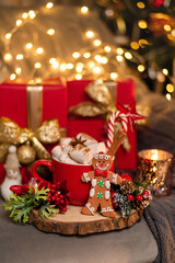 Beautiful Christmas gift boxes with a mug of hot cocoa drink with marshmallows and sweets on the floor near the Christmas tree in the room.