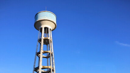 A concrete water tank on a tall tower. Large outdoor blue water tank for water supply systems in villages or urban communities. On a bright blue sky background with copy space. Selective focus