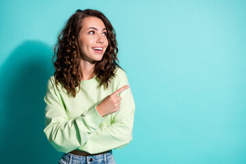 Photo portrait of excited woman pointing at blank space isolated on vivid turquoise colored background
