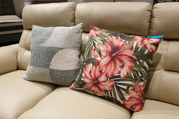 Close up of floral pattern throw pillow on a leather sofa with pillows in a furniture display warehouse.