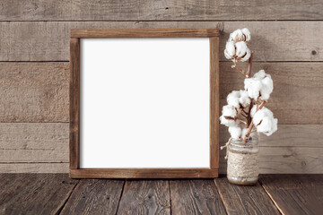 Rough square wooden frame with cotton branch on wooden background