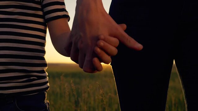 Happy, friendly family. Mother holds the hands of a little son. Hands of parent and child large in the light of a beautiful sunset. Teamwork. Way to success.
