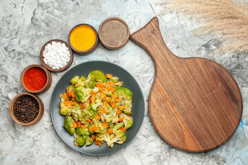 Horizontal view of healthy vegetable salad different spices and cutting board on white background