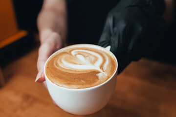 A large white cup of cappuccino in hand - an espresso-based Italian coffee drink with the addition of warmed frothed milk