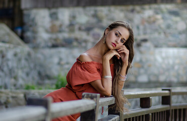 Beautiful young brunette woman with orange dress on a street urban background