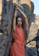 Beautiful young brunette woman with orange dress on a rock nature background