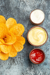 Vertical view of homemade potato chips decorated like flower shaped and salt with ketchup mayonnaise on gray background